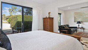 A bedroom with a large bed, a wooden dresser, a black leather sofa, and a dining table with chairs. There is a sliding glass door leading to a garden. - Hideaway Nook by Wine Coast Holiday Rentals (WHITES VALLEY)