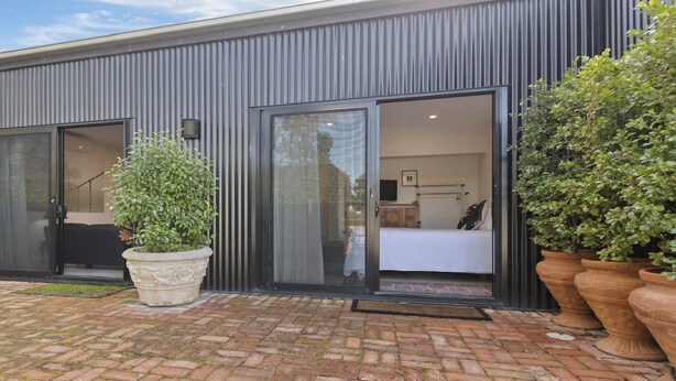 A modern building with two large sliding glass doors leading to a bedroom with a bed and a desk. There are potted plants on the ground. - Hideaway Nook by Wine Coast Holiday Rentals (WHITES VALLEY)