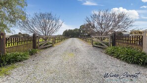 A gravel driveway leading to a gated entrance with a wooden fence and trees on either side. - Hideaway Nook by Wine Coast Holiday Rentals (WHITES VALLEY)