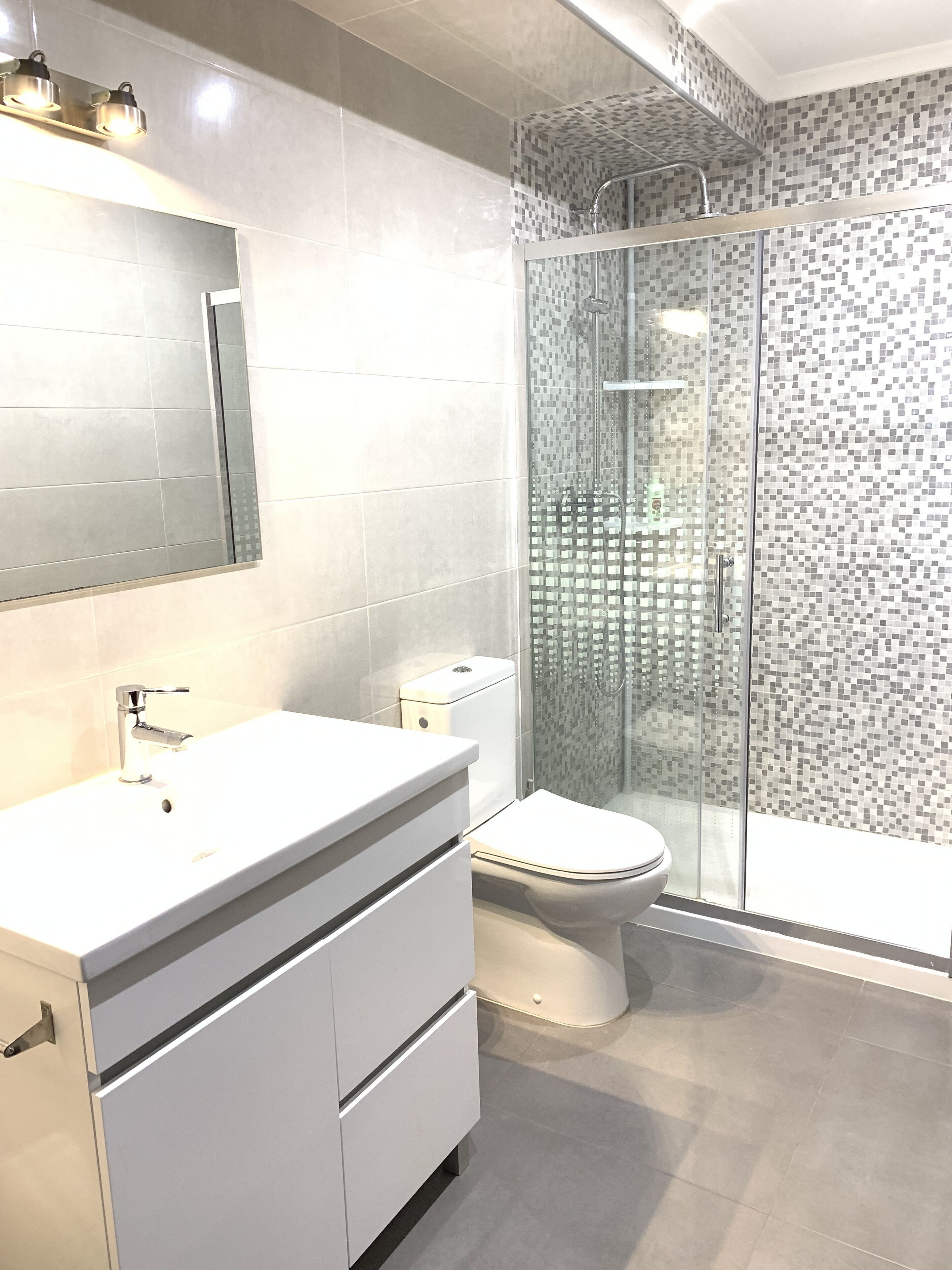 A modern bathroom with a white vanity, a toilet, and a glass-enclosed shower area.