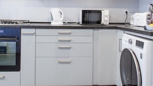 A modern kitchen with white cabinets, a microwave, a kettle, a toaster, and a washing machine.