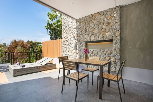 An outdoor patio with a stone wall, a wooden table, and chairs. - Scenic Green Hill Views 4BR Villa Jeanny (Kamala)