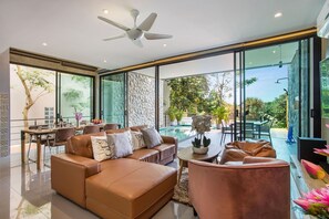 A modern living room with a brown leather sofa, a pink armchair, and a dining area with a table and chairs. - Scenic Green Hill Views 4BR Villa Jeanny (Kamala)