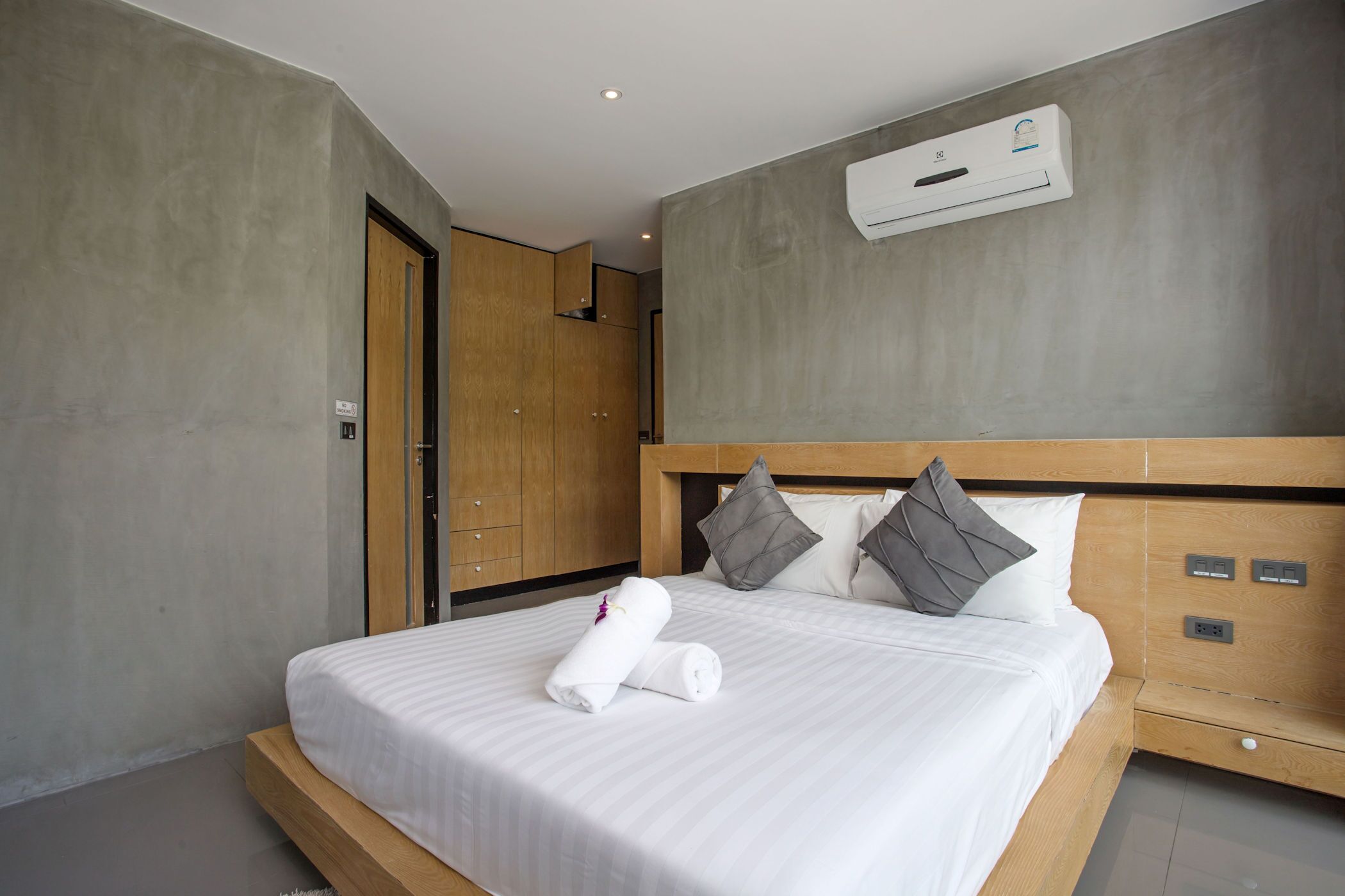 Quarto de hotel moderno com uma cama grande, cabeceira de madeira e unidade de ar condicionado integrada.
