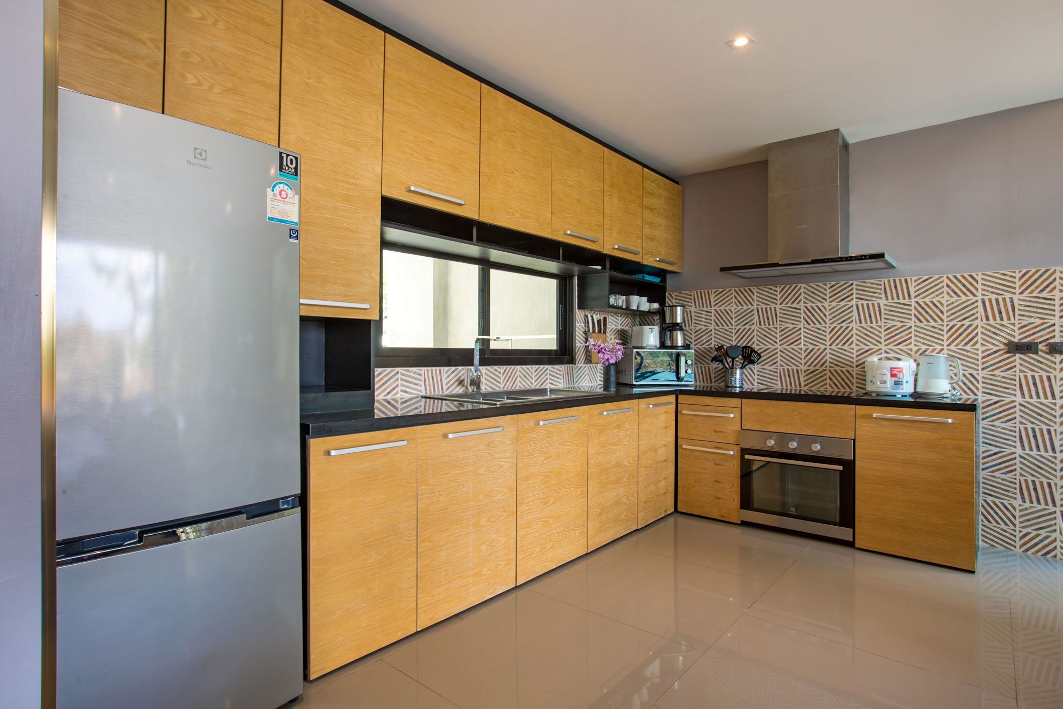 A modern kitchen with wooden cabinets, a stainless steel refrigerator, a built-in oven, and a patterned backsplash.