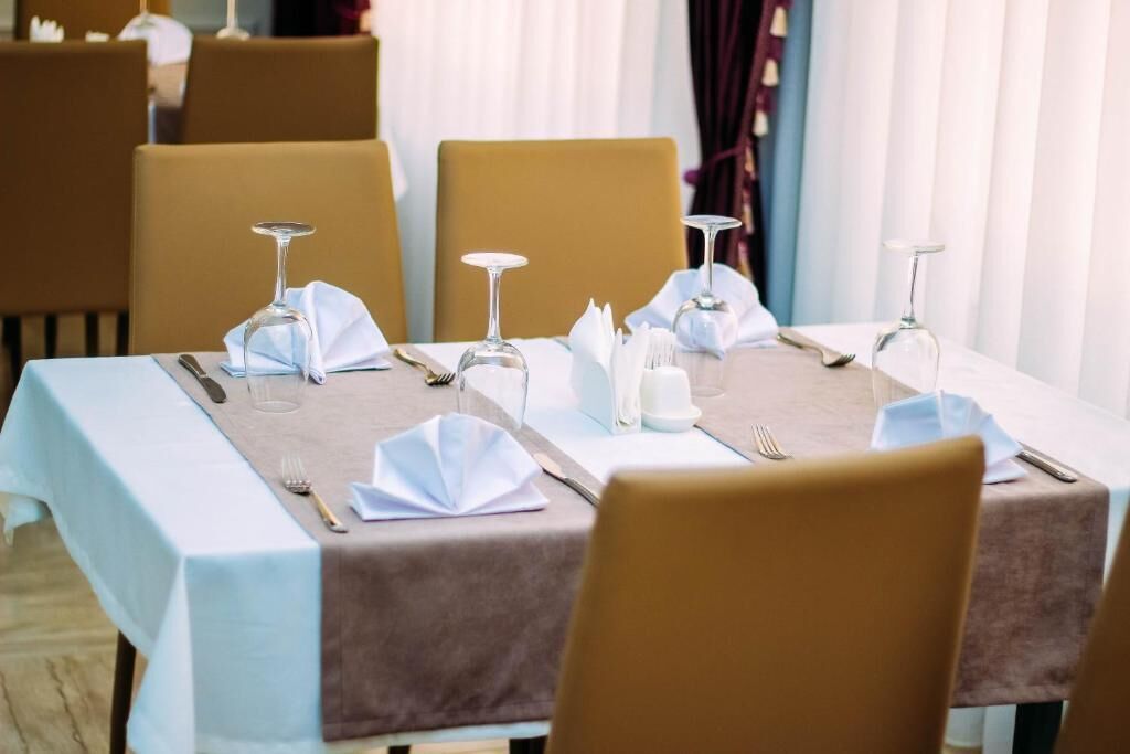 A dining table set with white napkins, cutlery, and wine glasses, surrounded by chairs.