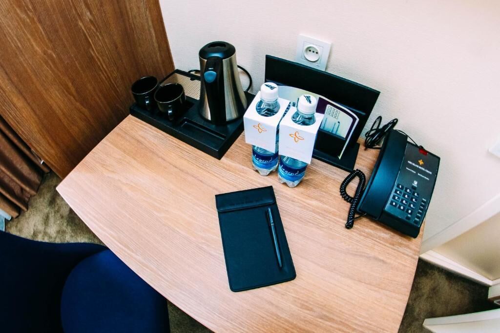 A hotel room desk with a coffee maker, two water bottles, a phone, and a black notebook.