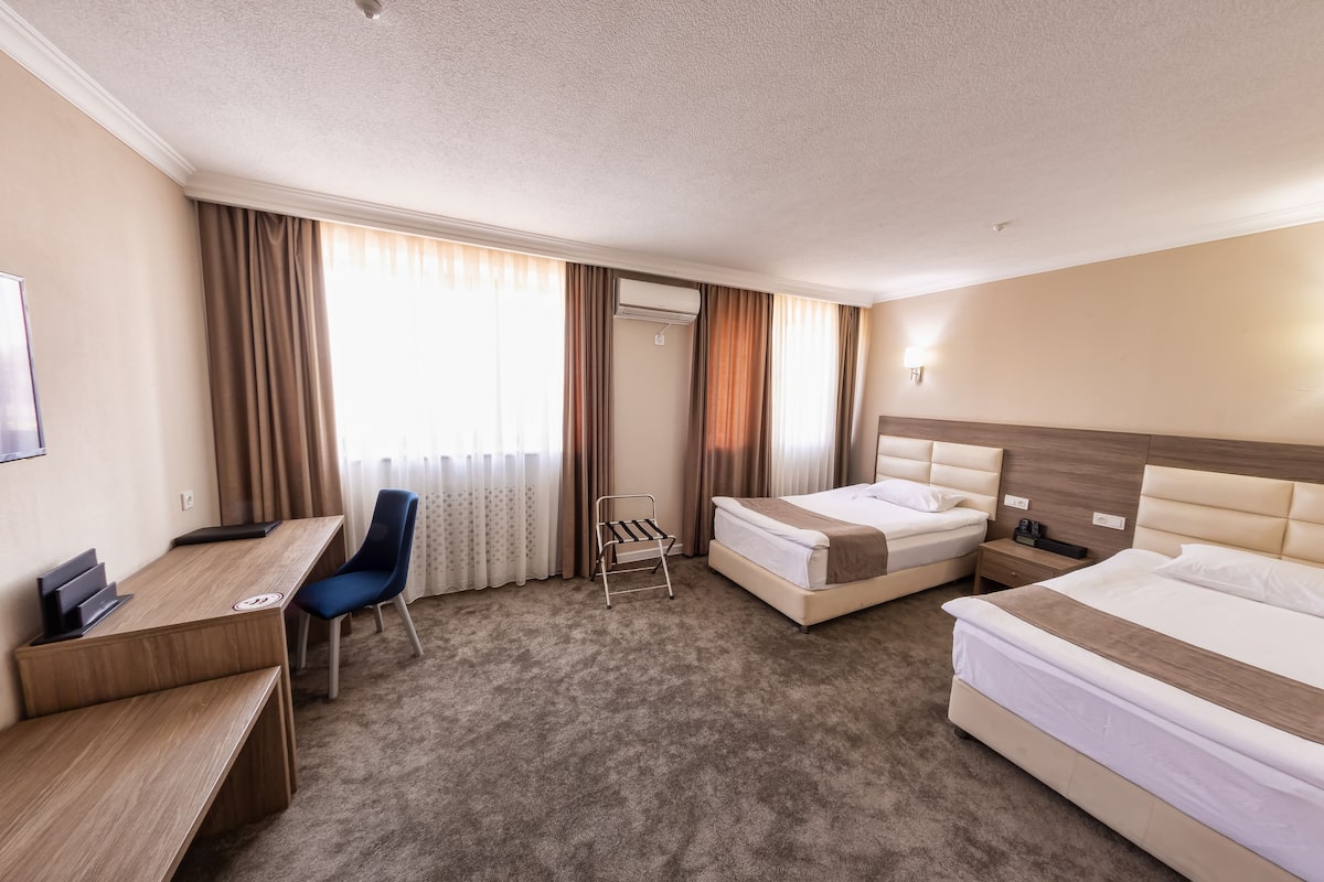 A hotel room with a desk, two beds, a chair, and a small table.
