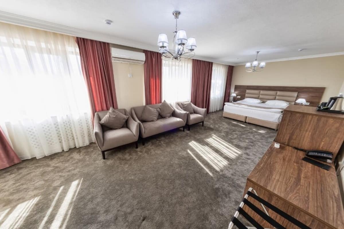 A hotel room with a large bed, a sofa, a wooden desk, and a chandelier.