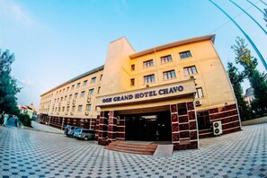 Exterior del hotel OSH Grand Chavo, con una entrada de azulejos y un coche estacionado.