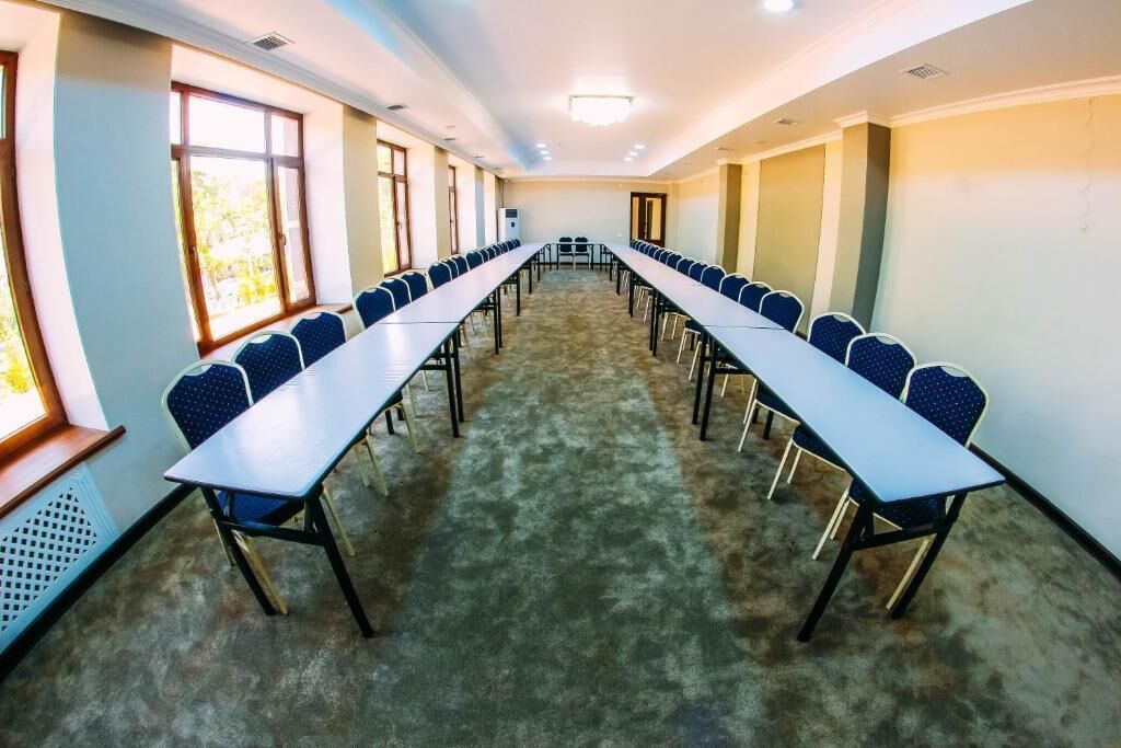 A conference room with long tables and chairs, large windows, and a carpeted floor.