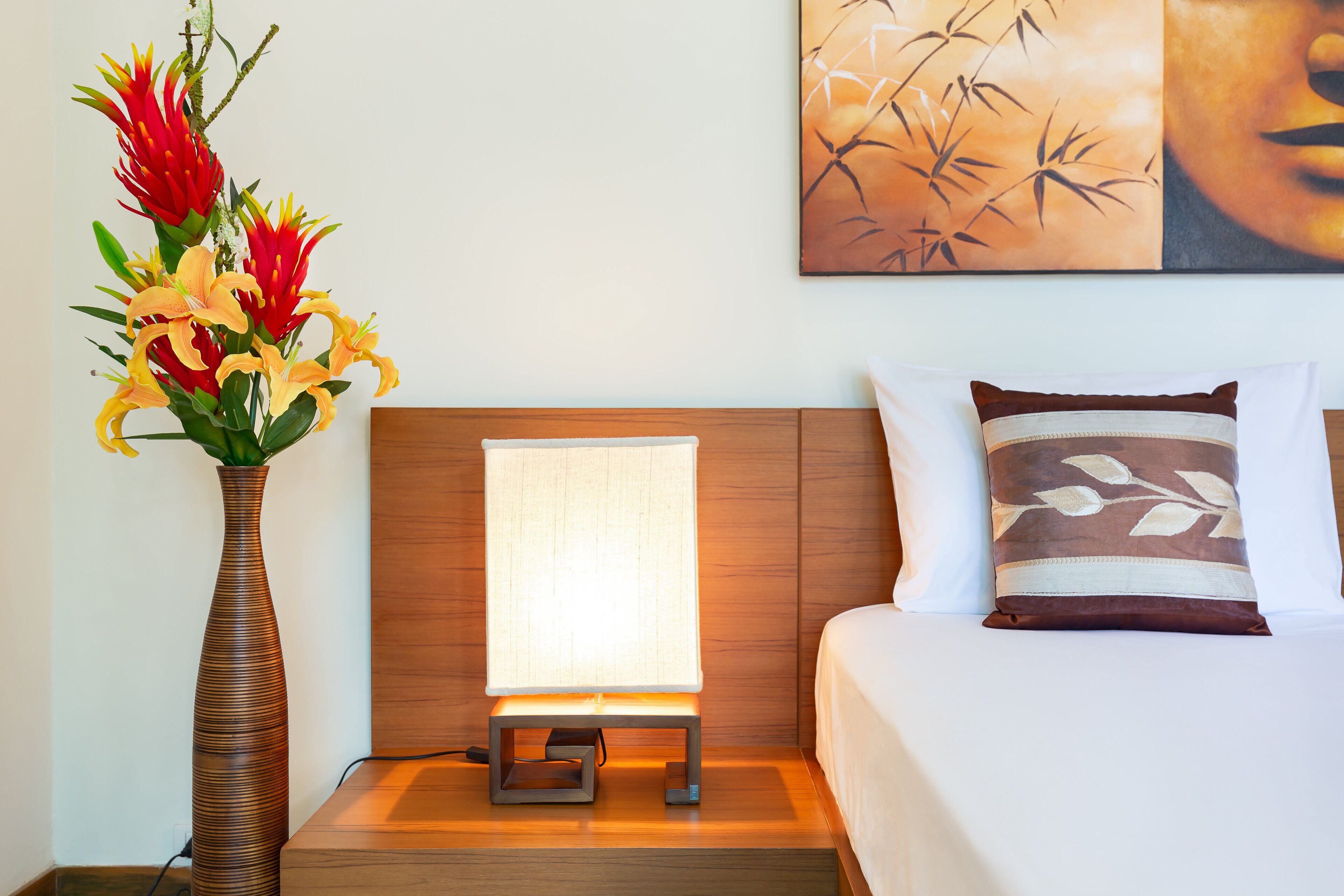 A hotel room with a bed, a nightstand with a lamp, and a vase of flowers.