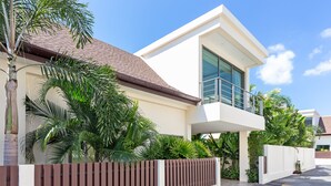 A modern two-story house with a balcony, surrounded by lush greenery and a gated driveway. - Two Storey Villa Kael in KA Villas Rawai (Rawai)