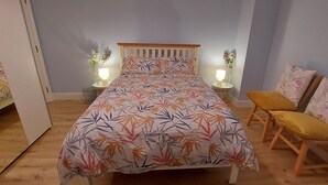 Quarto com cama, duas mesas de cabeceira com luminárias, uma cadeira e um espelho.