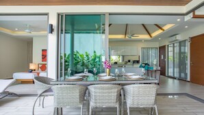 A modern dining area with a glass-top table, wicker chairs, and a view of the kitchen and living area. - Trendy 4BR Villa Kari in KA Villas Rawai (Rawai)
