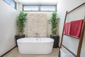 Ein modernes Badezimmer mit einer freistehenden Badewanne, zwei Topfpflanzen, einer Ziegelwand und einer Holzleiter mit einem Handtuch.