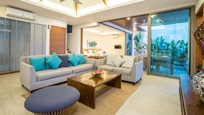 A modern living room with a sofa, coffee table, and a view of a balcony with plants. - Trendy 4BR Villa Kari in KA Villas Rawai (Rawai)