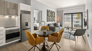 Una cocina moderna con electrodomésticos integrados, un comedor con una mesa redonda y sillas, y una sala de estar con un sofá y un ventanal amplio.
