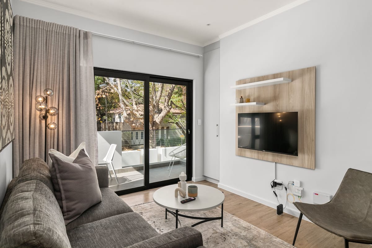 A modern living room with a grey sofa, a coffee table, and a flat-screen TV mounted on the wall.