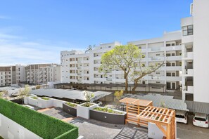 A modern residential building with multiple balconies, a rooftop garden, and a wooden pergola.