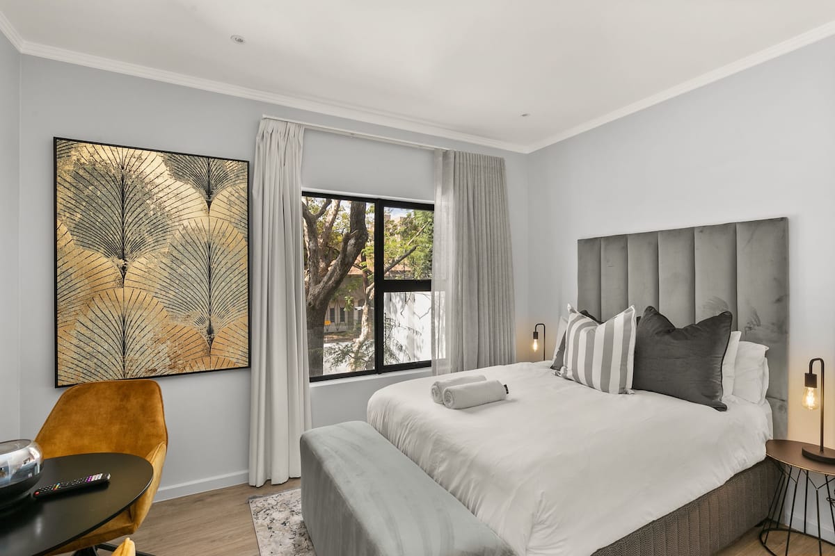 A modern bedroom with a large bed, a side table, a chair, and a window with curtains.
