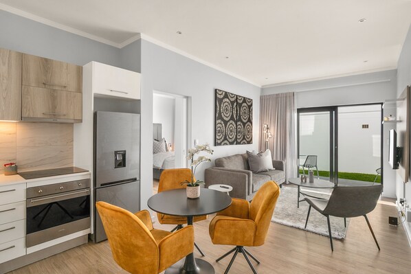 A modern kitchen with a built-in oven and refrigerator, a dining area with a round table and two chairs, and a living area with a sofa and a coffee table.