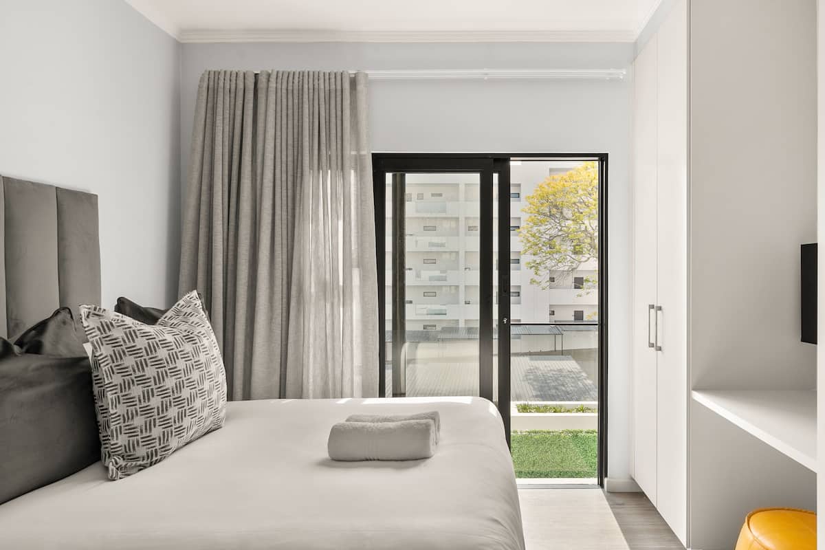 A modern hotel room with a large bed, a view of the city through a sliding door, and a small balcony.
