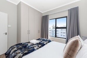 A hotel room with a bed, a large window, and a wardrobe.