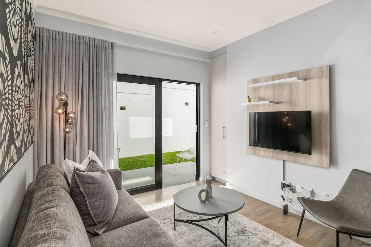 A modern living room with a grey sofa, a coffee table, and a flat-screen TV mounted on the wall.