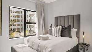 Una habitación de hotel moderna con una cama grande, vista al exterior del edificio y una lámpara de noche.