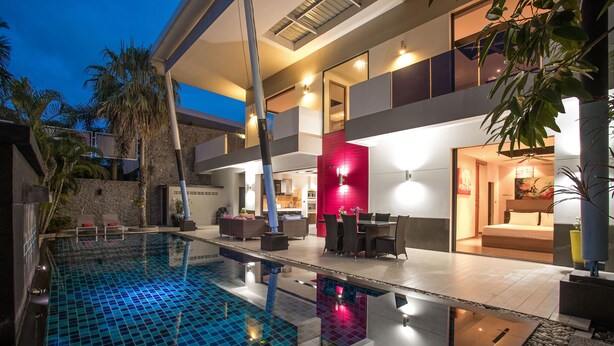 Una casa moderna con piscina, mobiliario de exterior y una pared de acento roja.