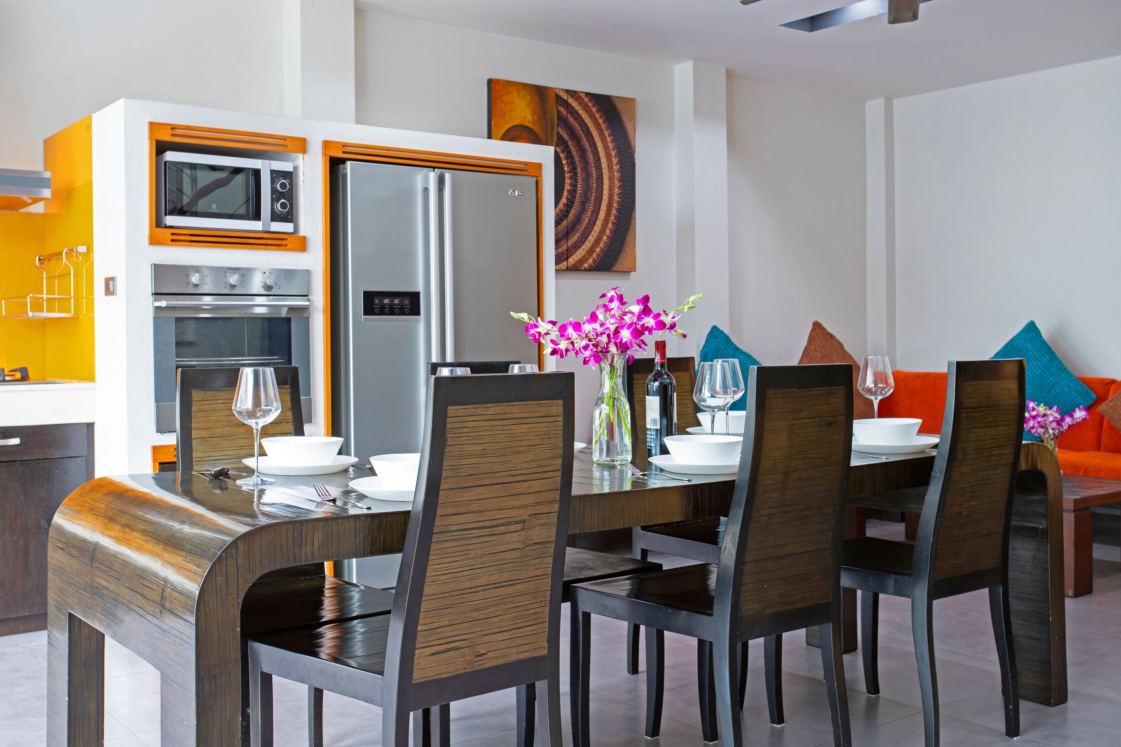 Un comedor moderno con cocina integrada, que incluye microondas, horno y refrigerador. Hay cuatro sillas alrededor de una mesa con un florero.