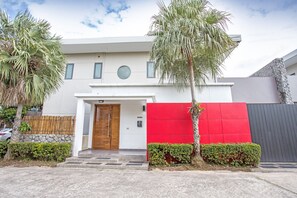 Uma casa moderna de dois andares com porta de madeira, parede de destaque vermelha e fachada de pedra.