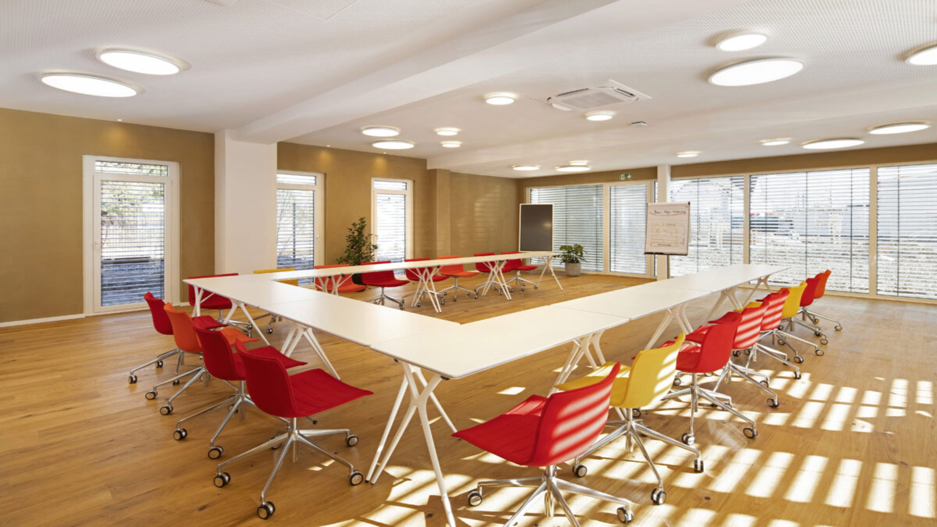 A conference room with a long table, red and yellow chairs, large windows, and a whiteboard.