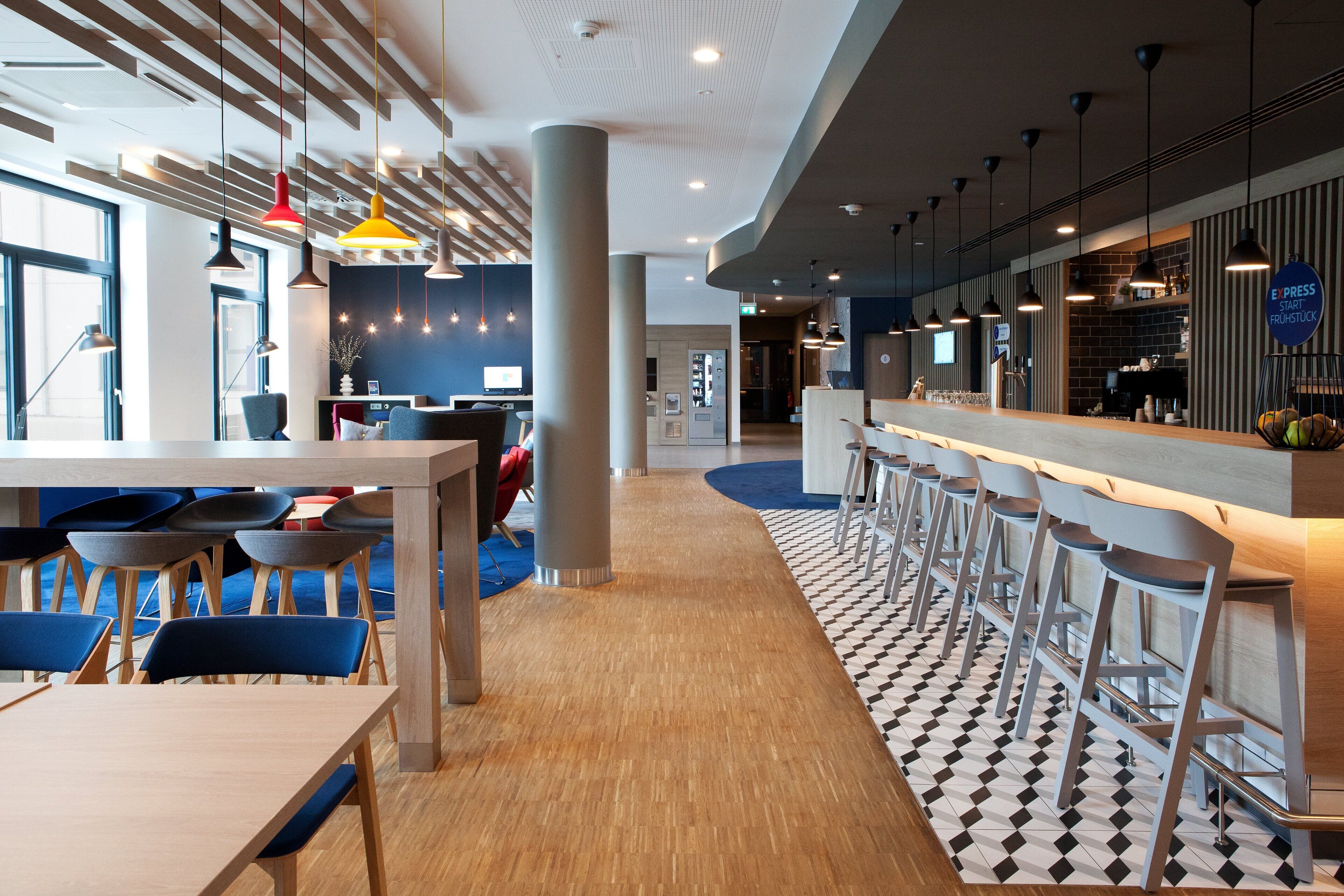 Un restaurante moderno con mesas altas, taburetes de bar, suelo estampado e iluminación colgante.