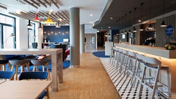 A modern restaurant with high tables and bar stools, a patterned floor, and pendant lighting.