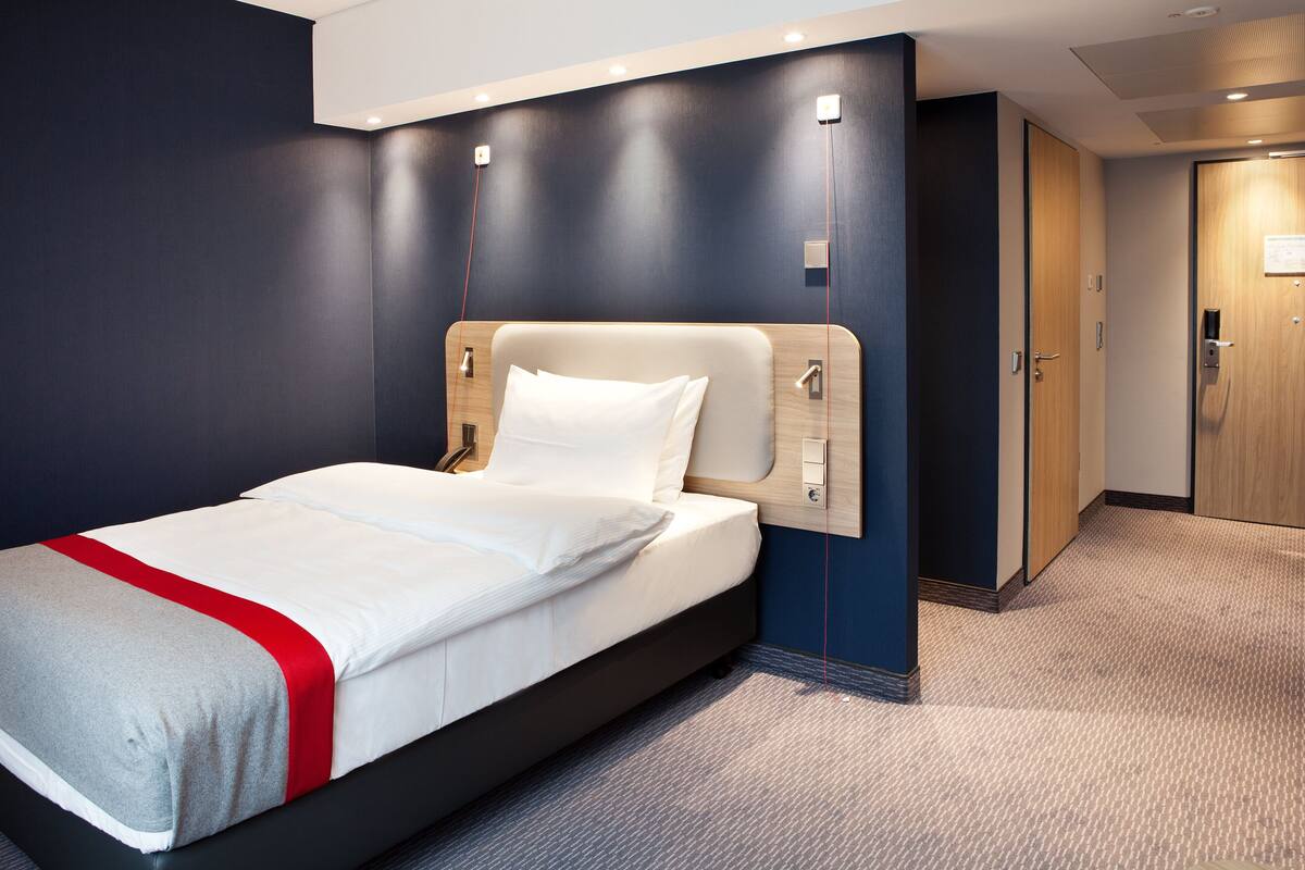 Una habitación de hotel moderna con una cama grande, paredes oscuras y una puerta de madera.