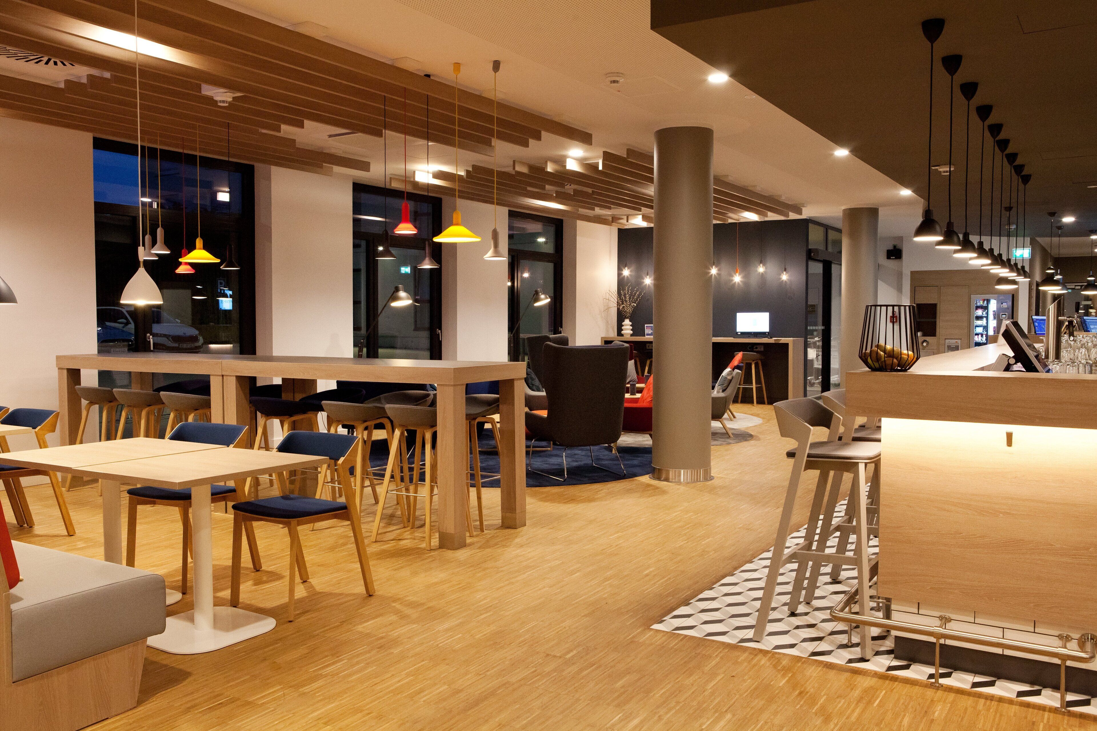 Un restaurante moderno con mesas y sillas de madera, iluminación colgante y una zona de bar.