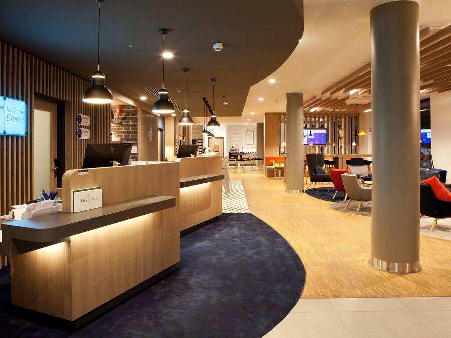 A modern hotel reception area with a wooden reception desk, multiple pendant lights, and a seating area with chairs and tables.