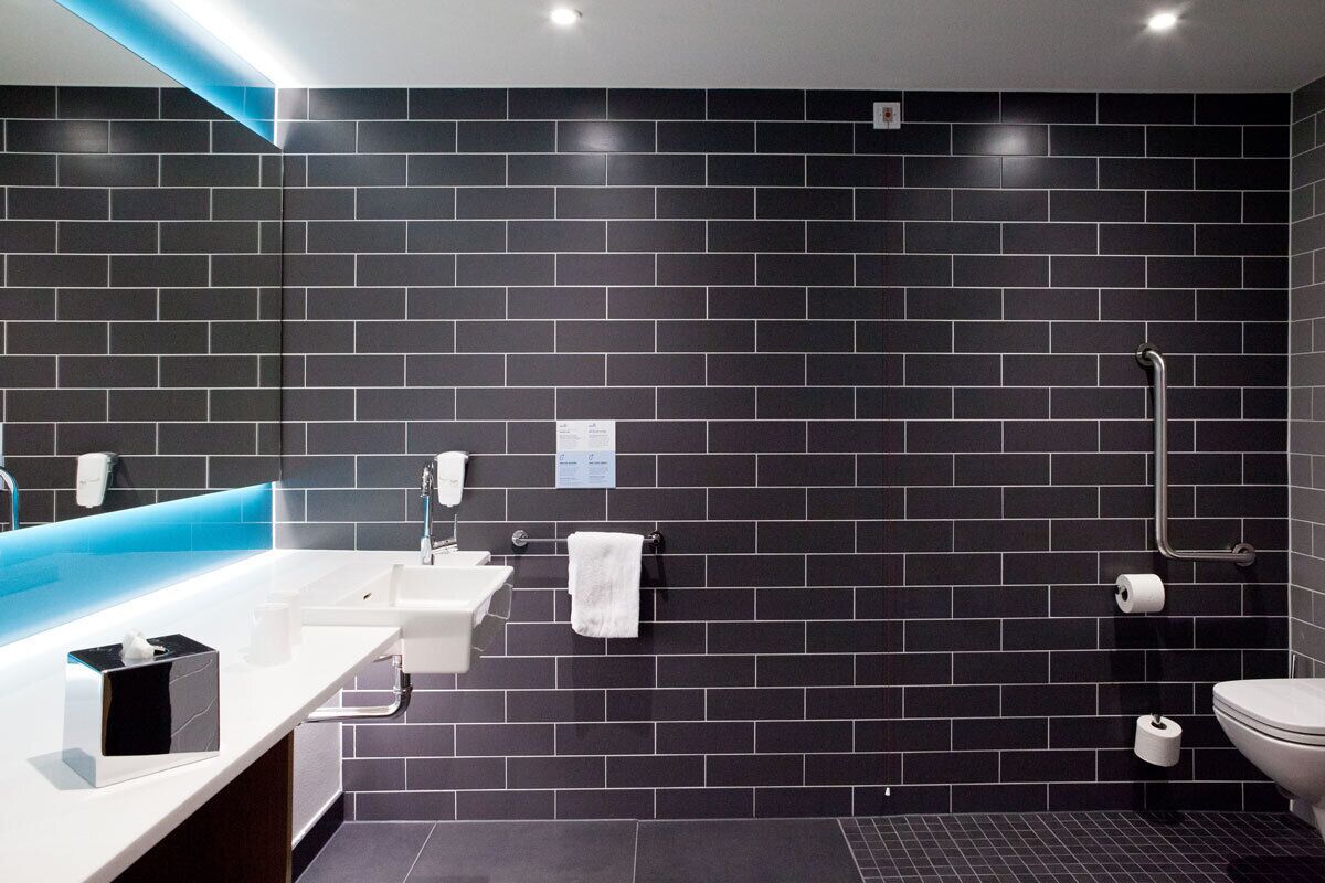 Un baño moderno con pared de azulejos negros, un lavabo blanco, un espejo y una ducha.
