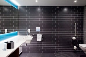 A modern bathroom with a black tiled wall, a white sink, a mirror, and a shower.