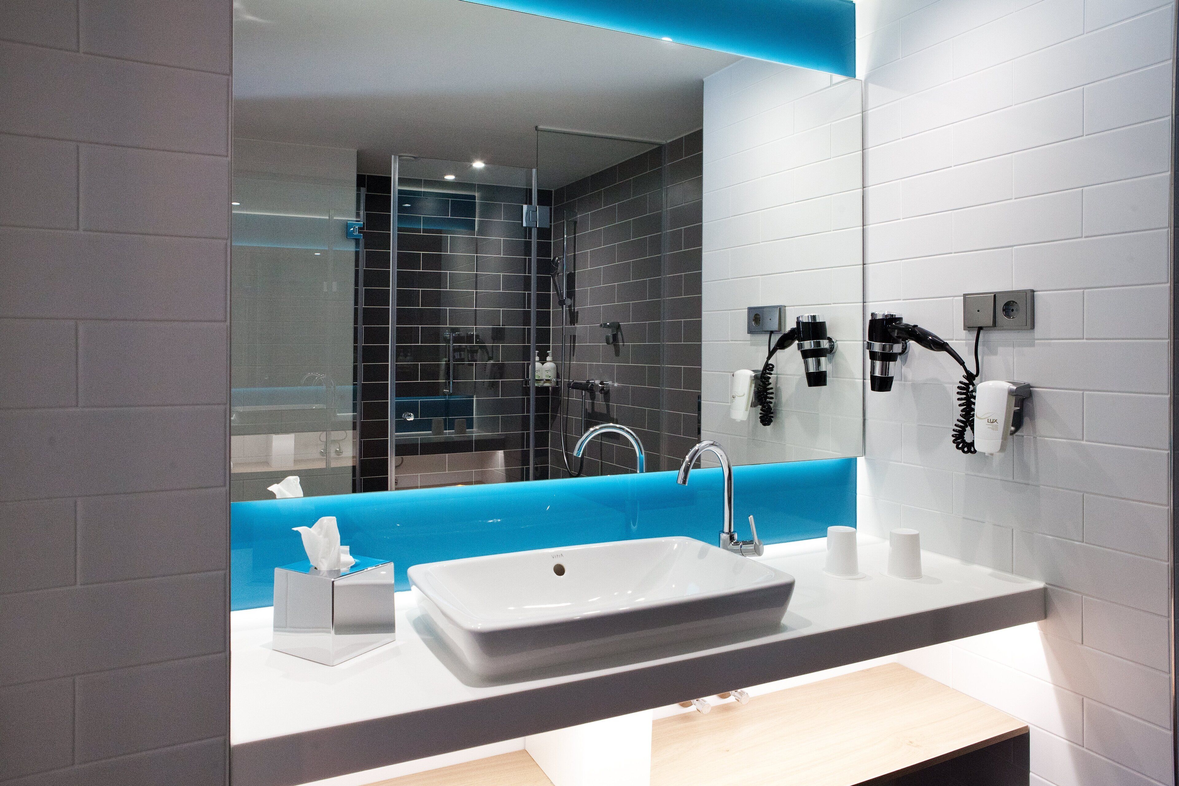 A modern bathroom with a large mirror, a white sink, and a blue accent wall.
