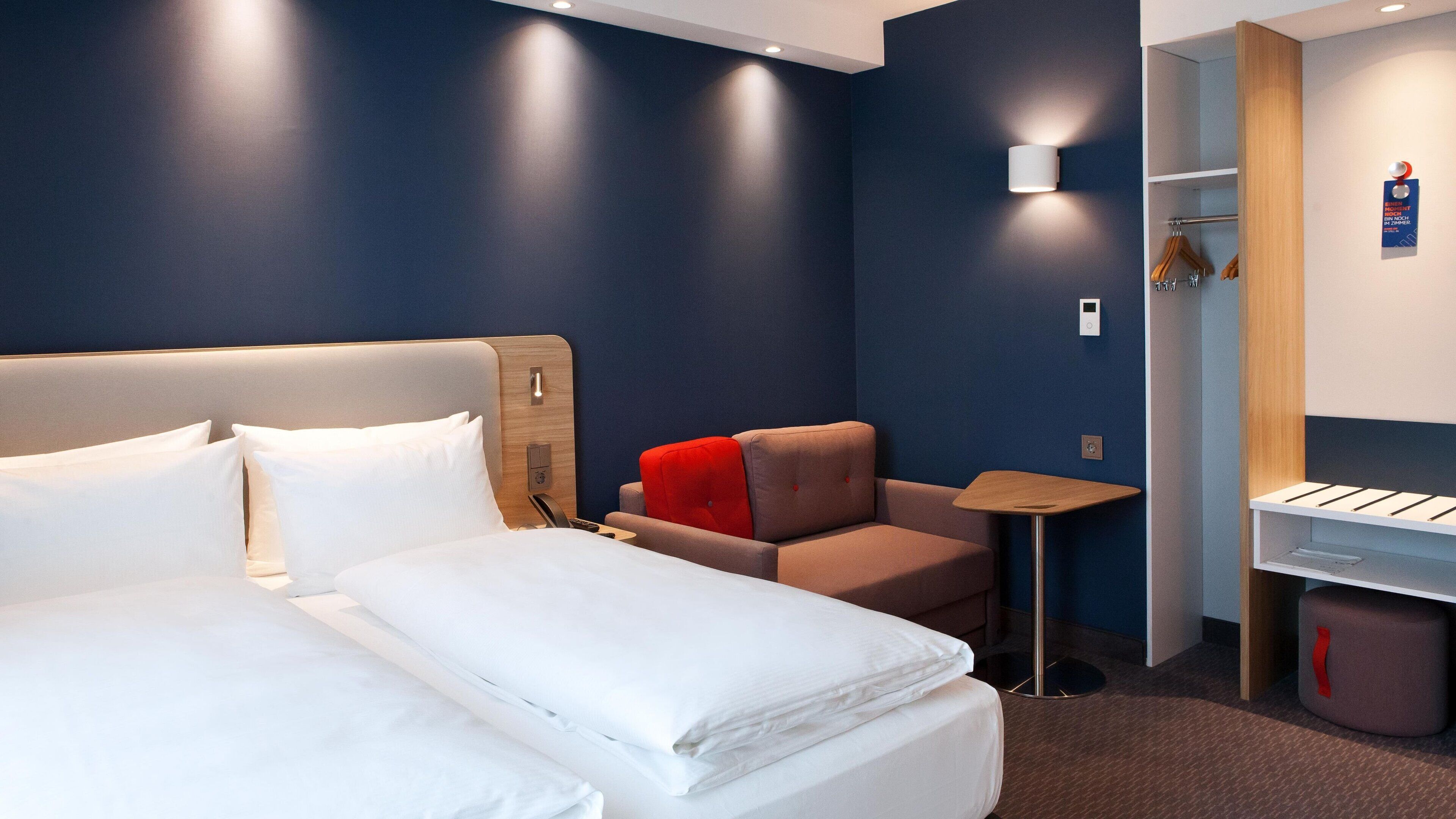 Una habitación de hotel con una cama grande, un sofá pequeño, una mesita auxiliar y un armario.