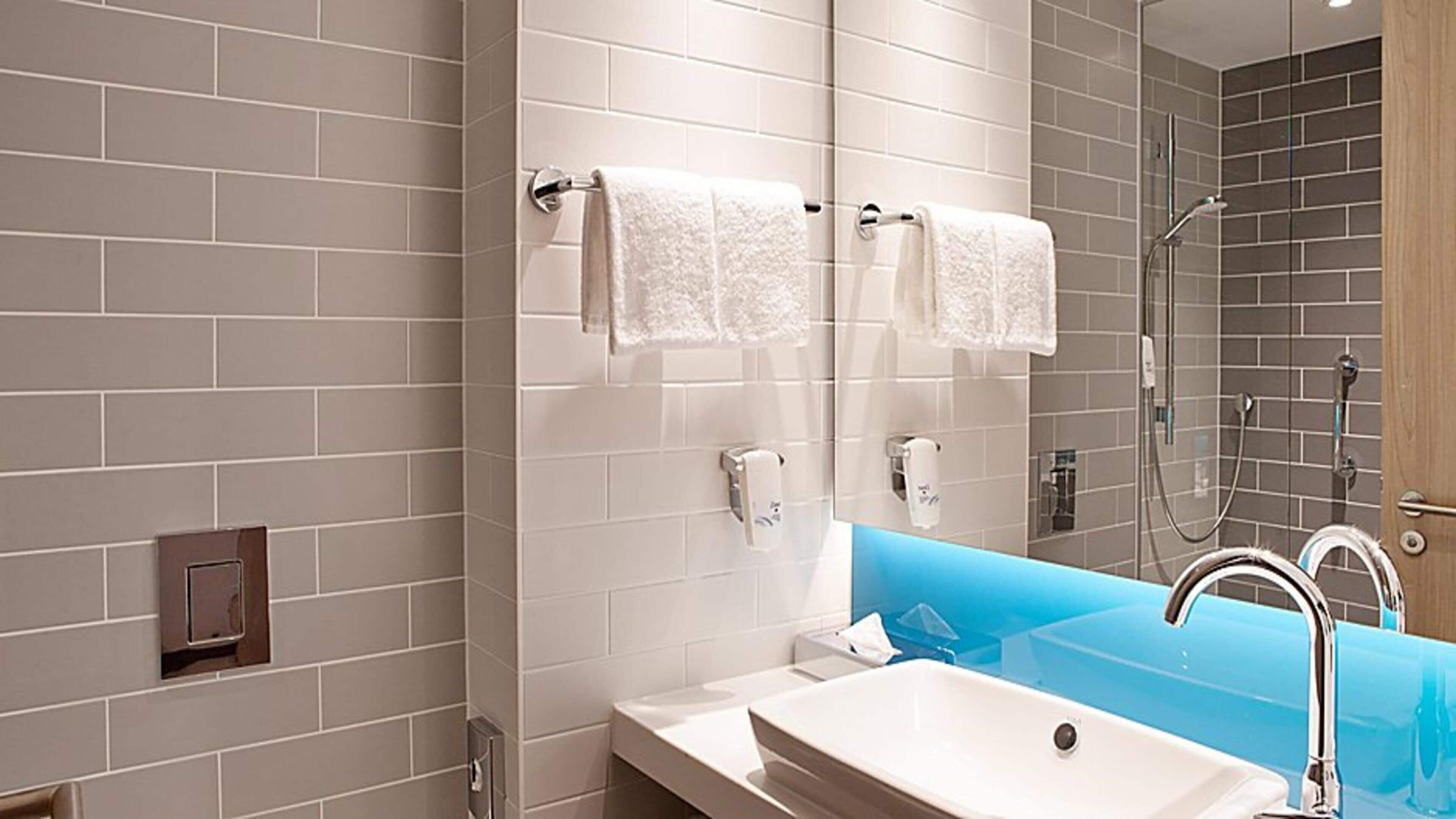 A modern bathroom with a white sink, a mirror, and a shower area.