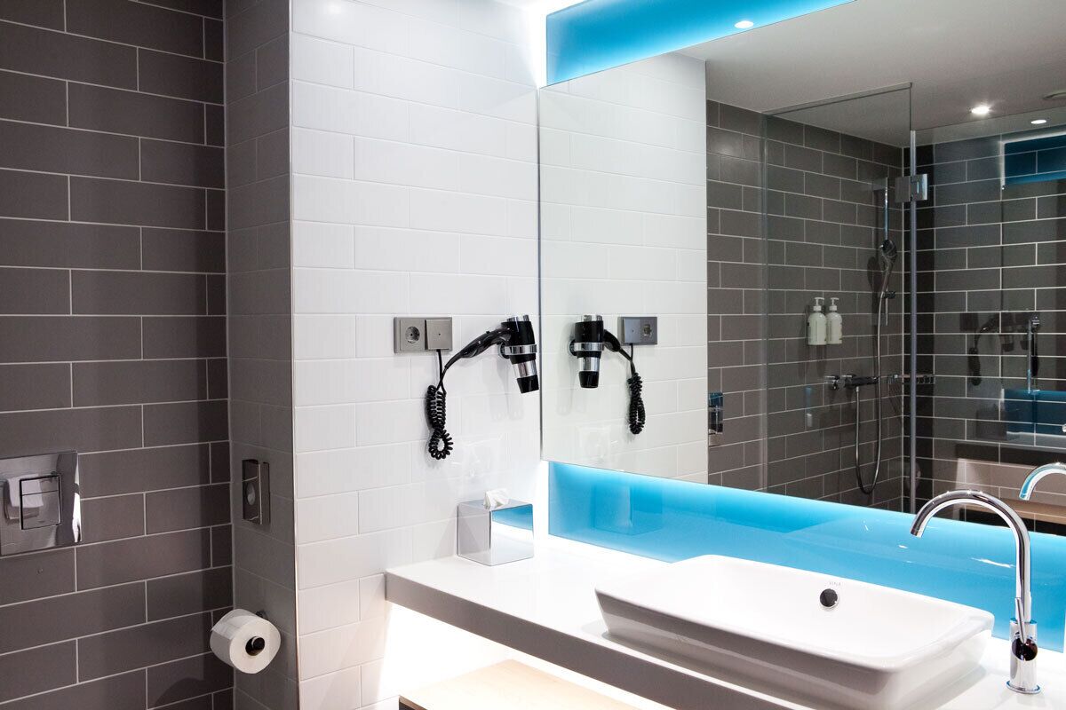A modern bathroom with a white sink, a large mirror, and a blue accent wall.