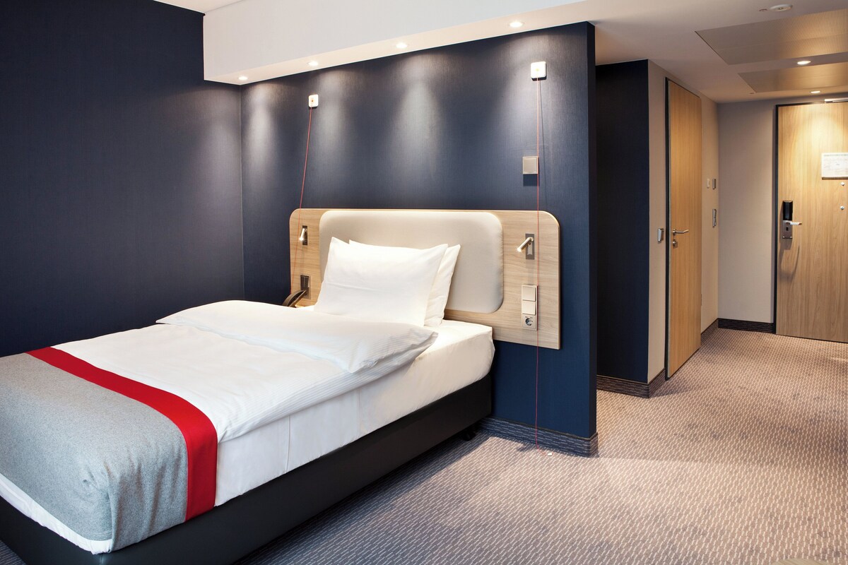 Een moderne hotelkamer met een groot bed, donkere wanden en een houten deur.