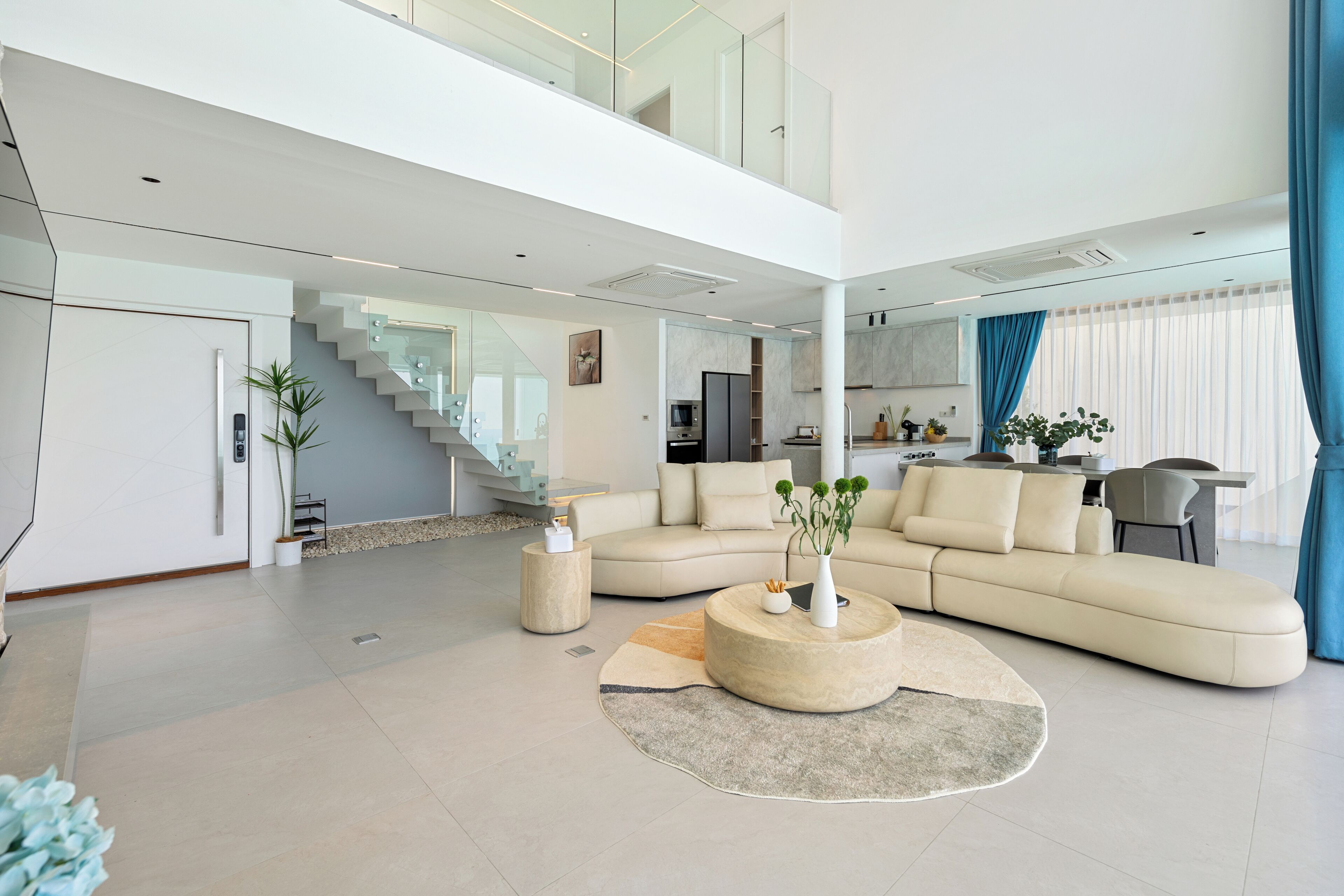 Un vaste espace de vie comprenant un grand canapé en forme de L, une table basse ronde et un escalier menant à un niveau supérieur.