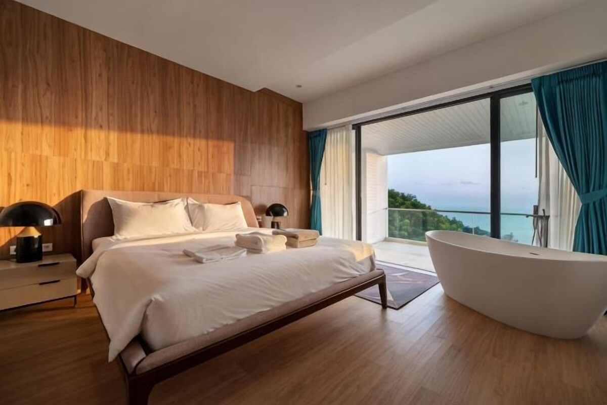 A modern bedroom with a large bed, a bathtub, and a balcony with a view.