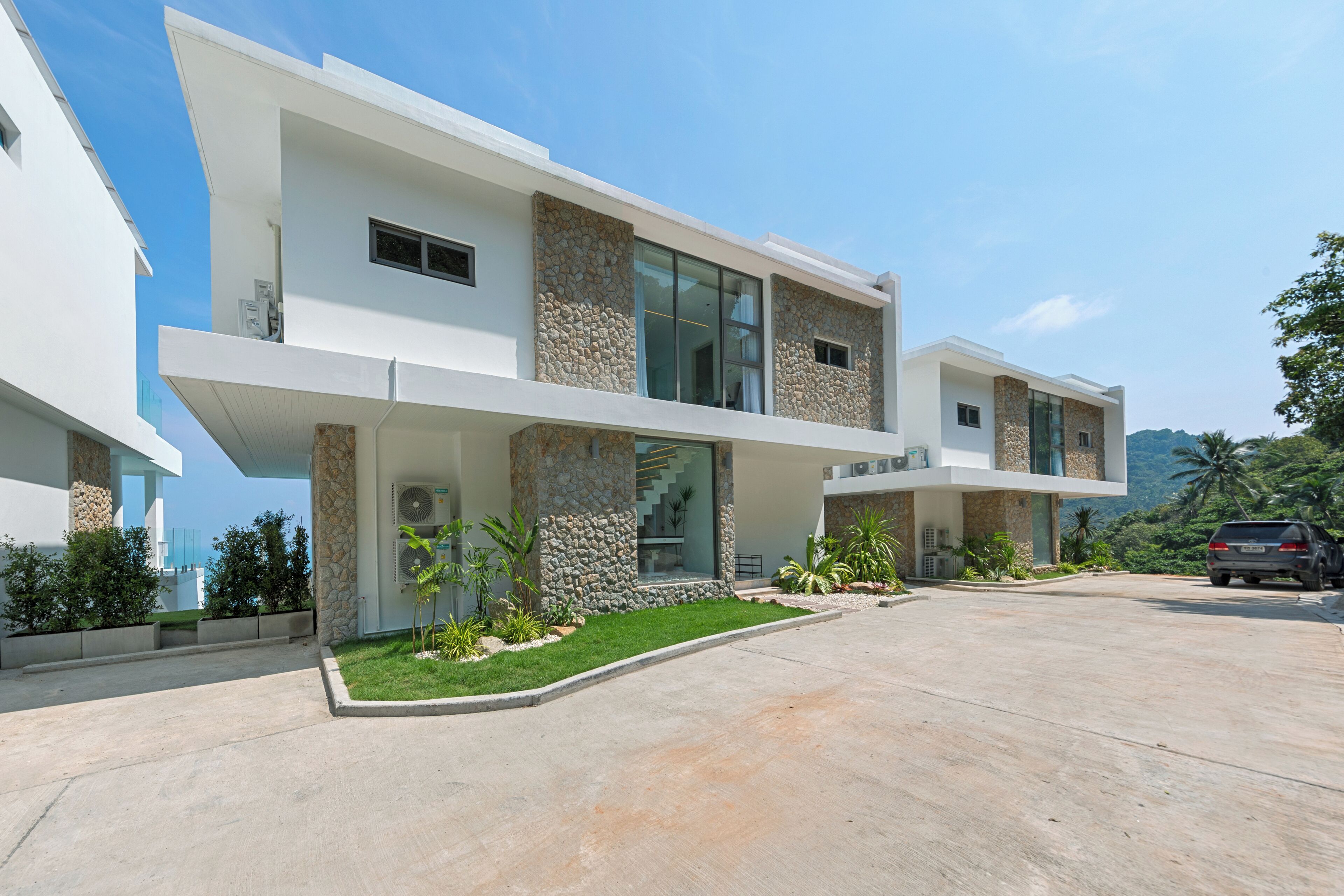 A modern multi-story house with a flat roof, large windows, and a stone facade.