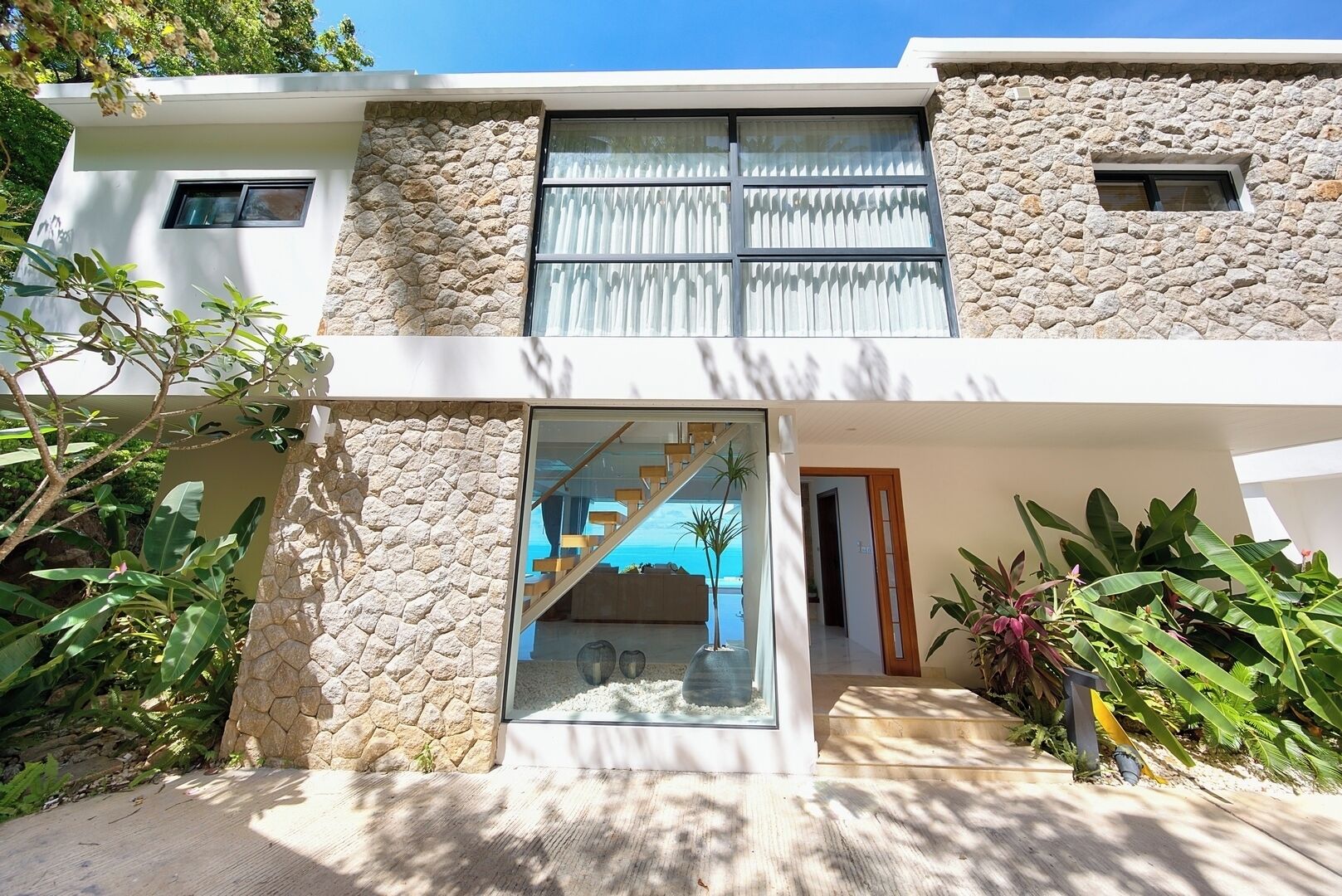 A modern two-story house with a stone facade, large windows, and a visible staircase leading to an upper level.